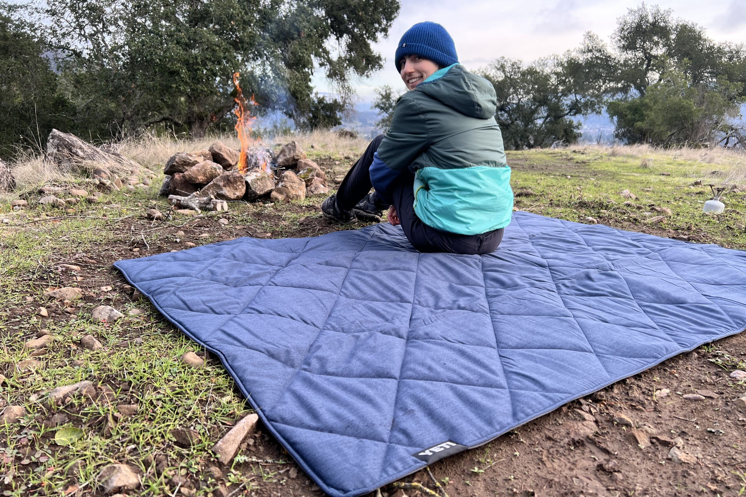 Women sitting on the Yeti Lowlands Blanket in front of a small campfire.