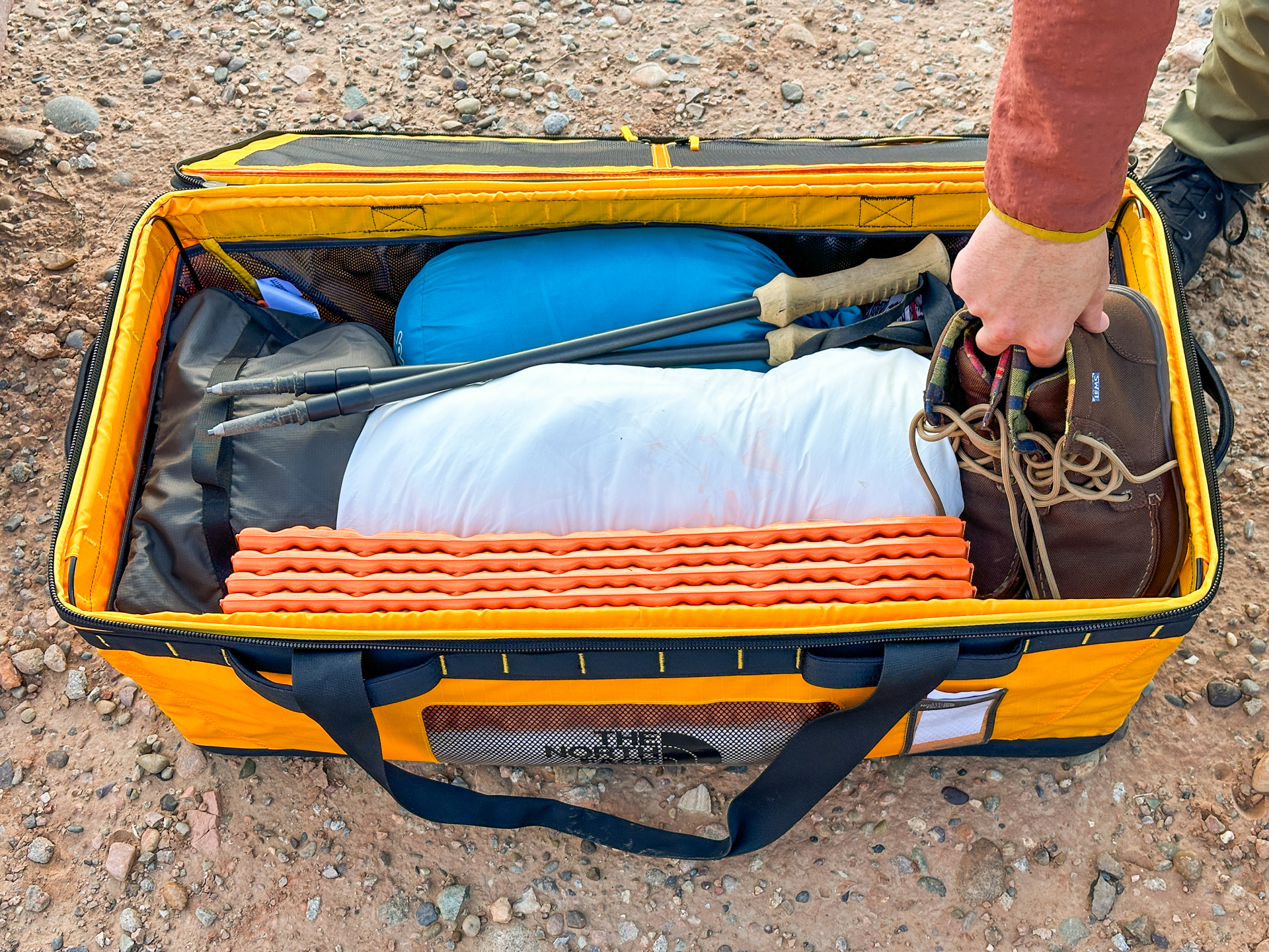 The Gear Box open and full of bulky camping gear, a hand pulls out a pair of hiking boots.