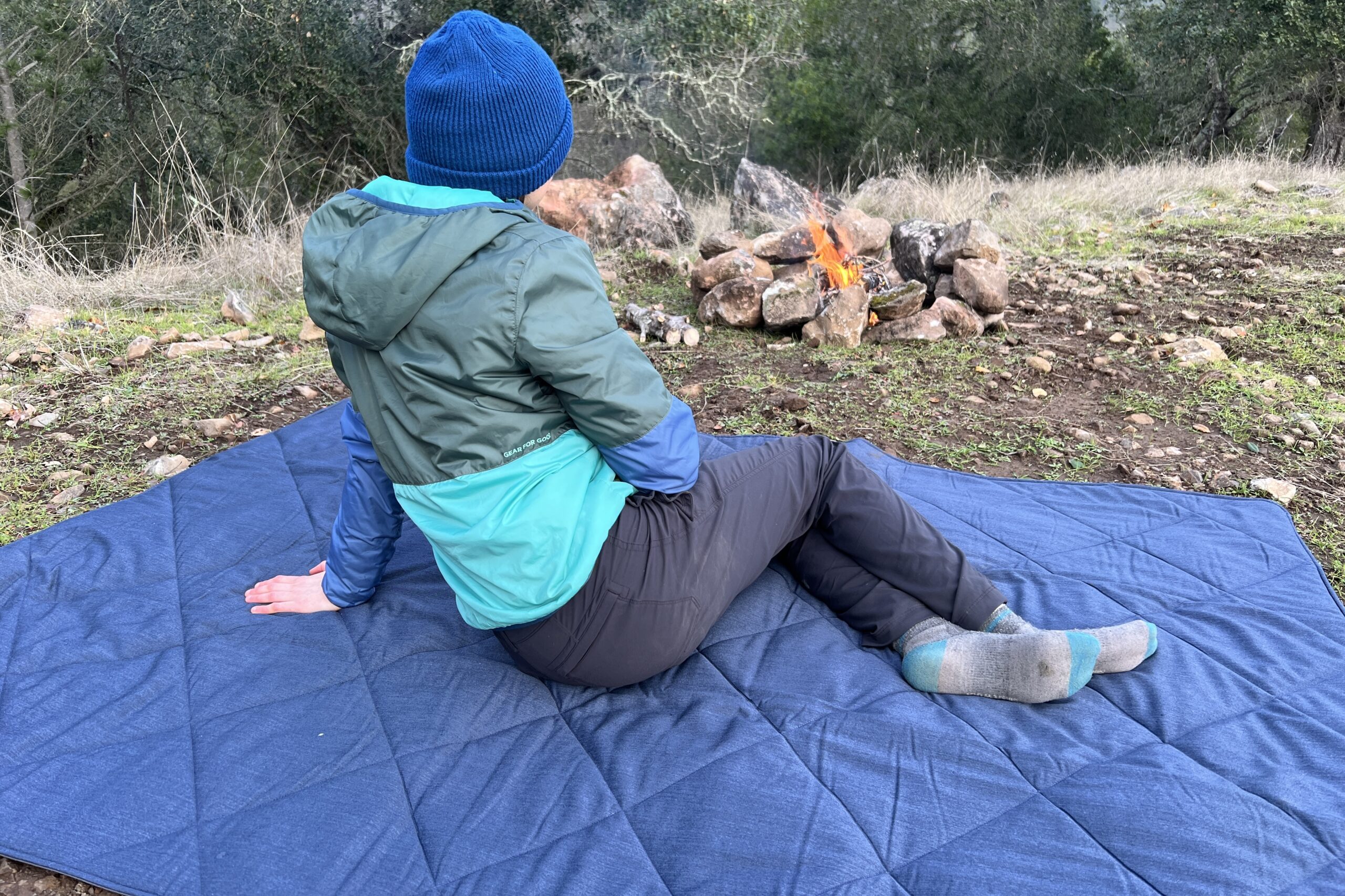 Women laying on her side on the Yeti Lowlands Blanket beside a small campfire.