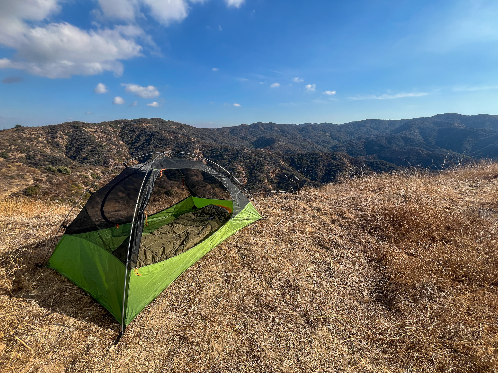 The Clostnature Polaris with the rainfly off and both doors open showing the interior of tent and a sleeping bag. Blue sky and rolling mountains in the background.