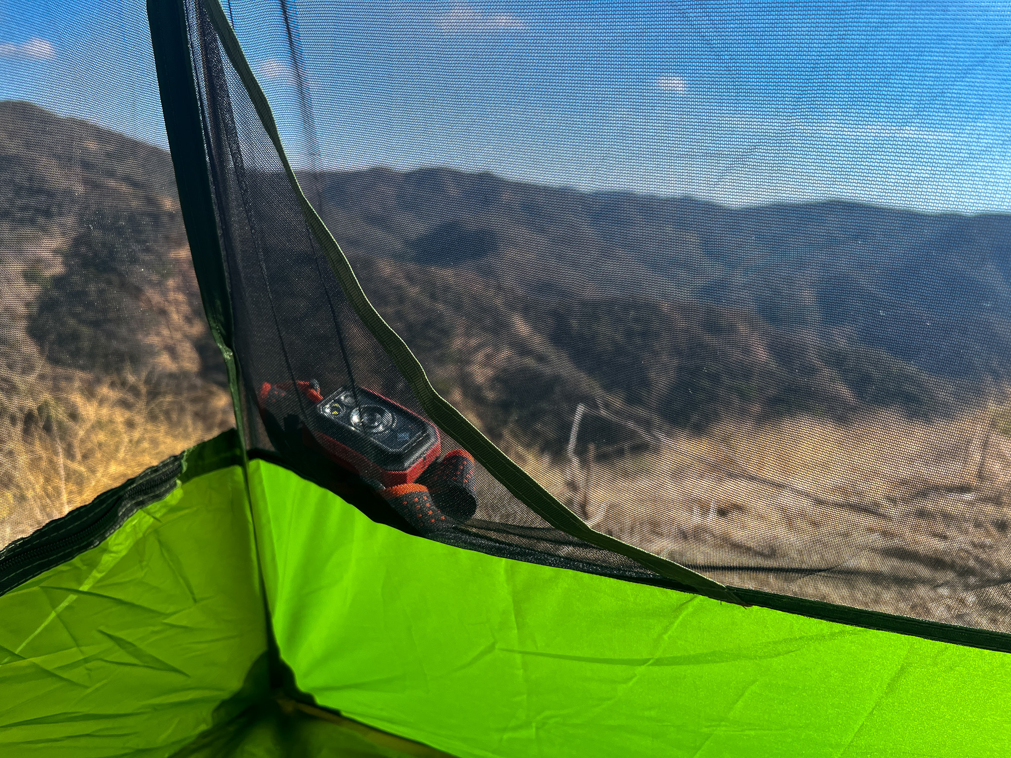 Closeup of one of the interior storage pockets on the Clostnature Polaris 2 with a headlamp inside, and the mountains visible in the background through the mesh.