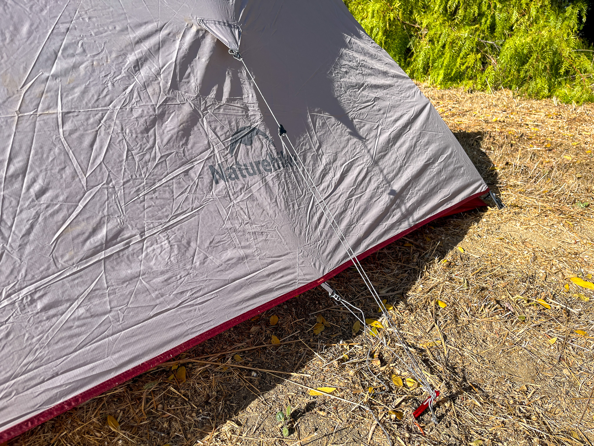 A closeup of the Naturehike CloudUp 2's rainfly, showing its waterproof nylon material and sturdy guy-out points. Part of a large tree is visible in the upper right corner.