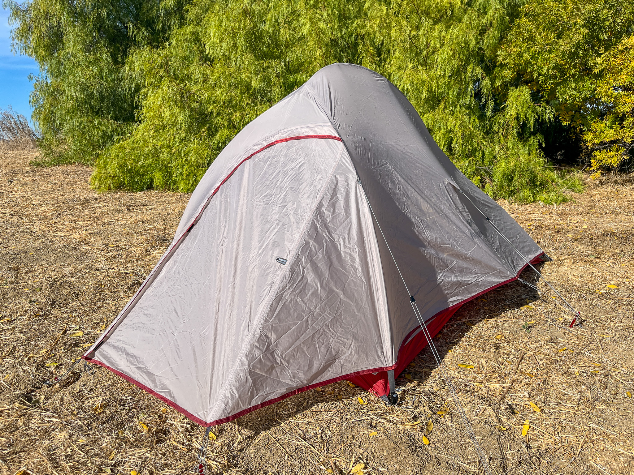 The Naturehike CloudUp 2 tent is pitched with the rainfly fully zipped and guyed out in a dirt clearing with a large tree in the background.