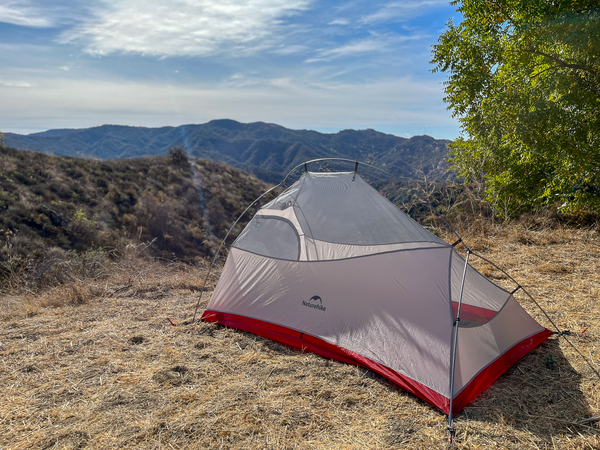 The Naturehike CloudUp 2 is set up without a rainfly, on a scenic mountain of the surrounding landscape. It's shown from a three quarter view from the back.