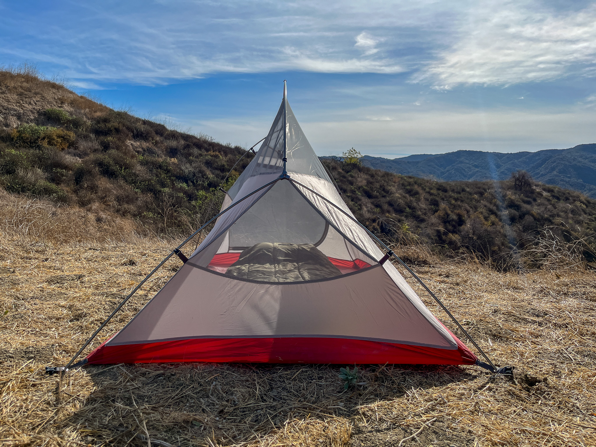 The Naturehike CloudUp 2 pitched on a hilltop, showcasing its unique profile from the rear. Rolling hills and blue sky are visible in the background.