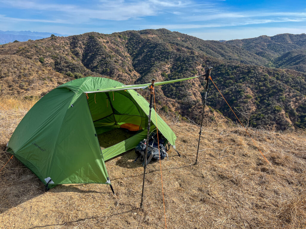 The Clostnature Polaris 2 pitched with doors open and the awning deployed and a backpack under the vestibule. Rolling mountains in the background.