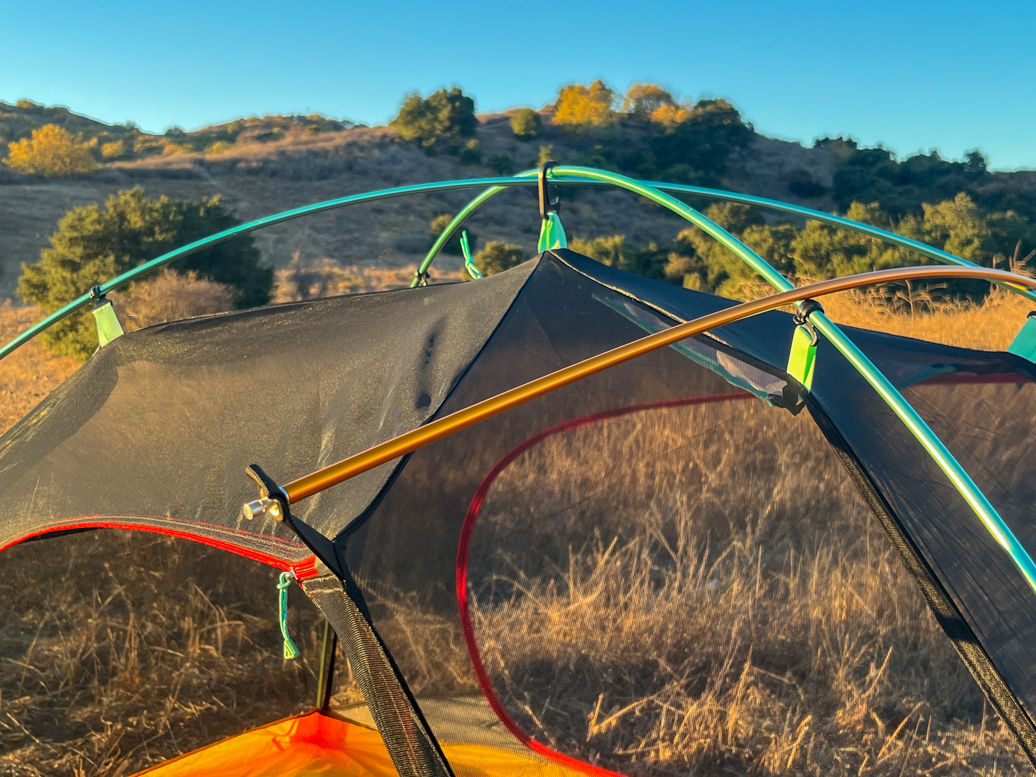 Detail shot of the top of the tent showing the two X-poles, ridgepole, and clip system. Rolling hills, blue sky, and bushes in the background.