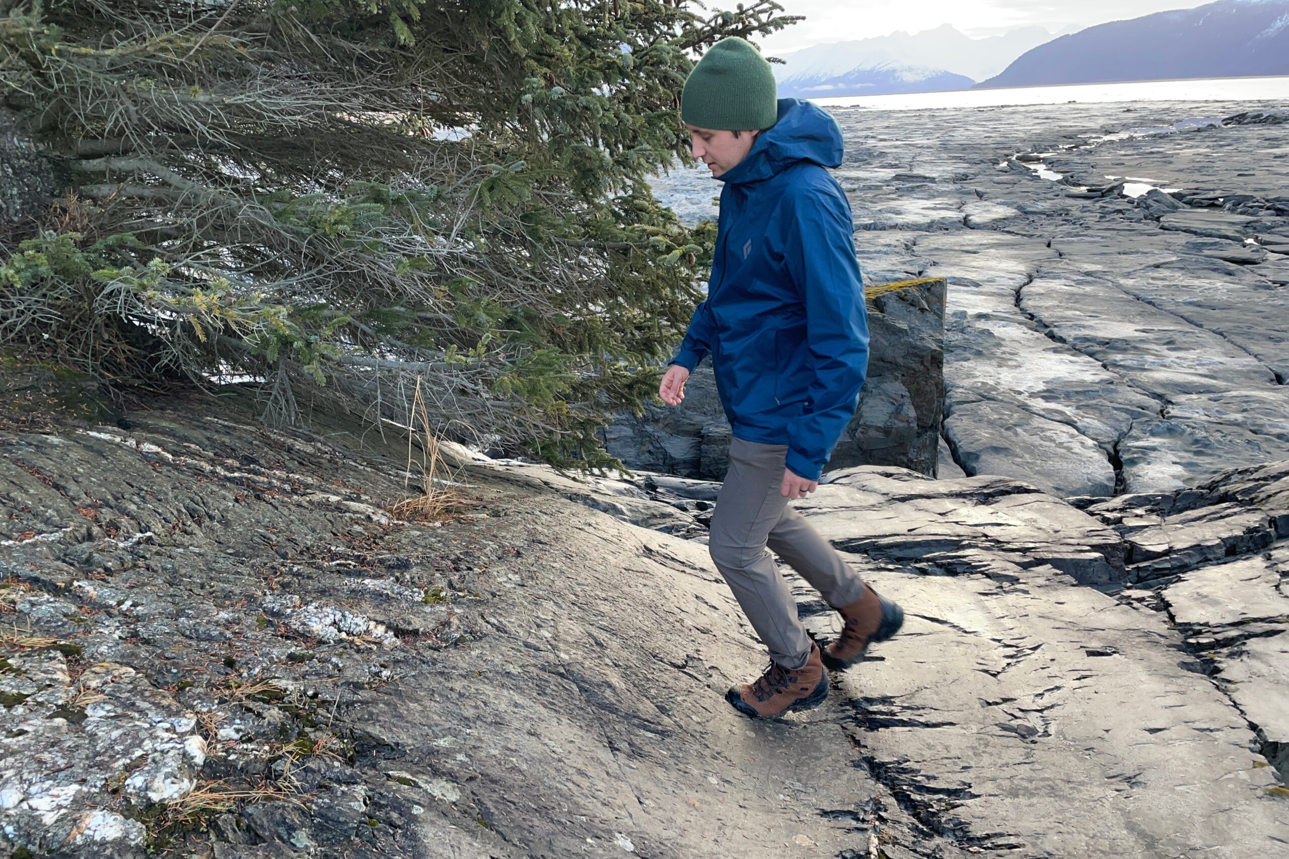 A man walks up a rocky slope above the ocean.