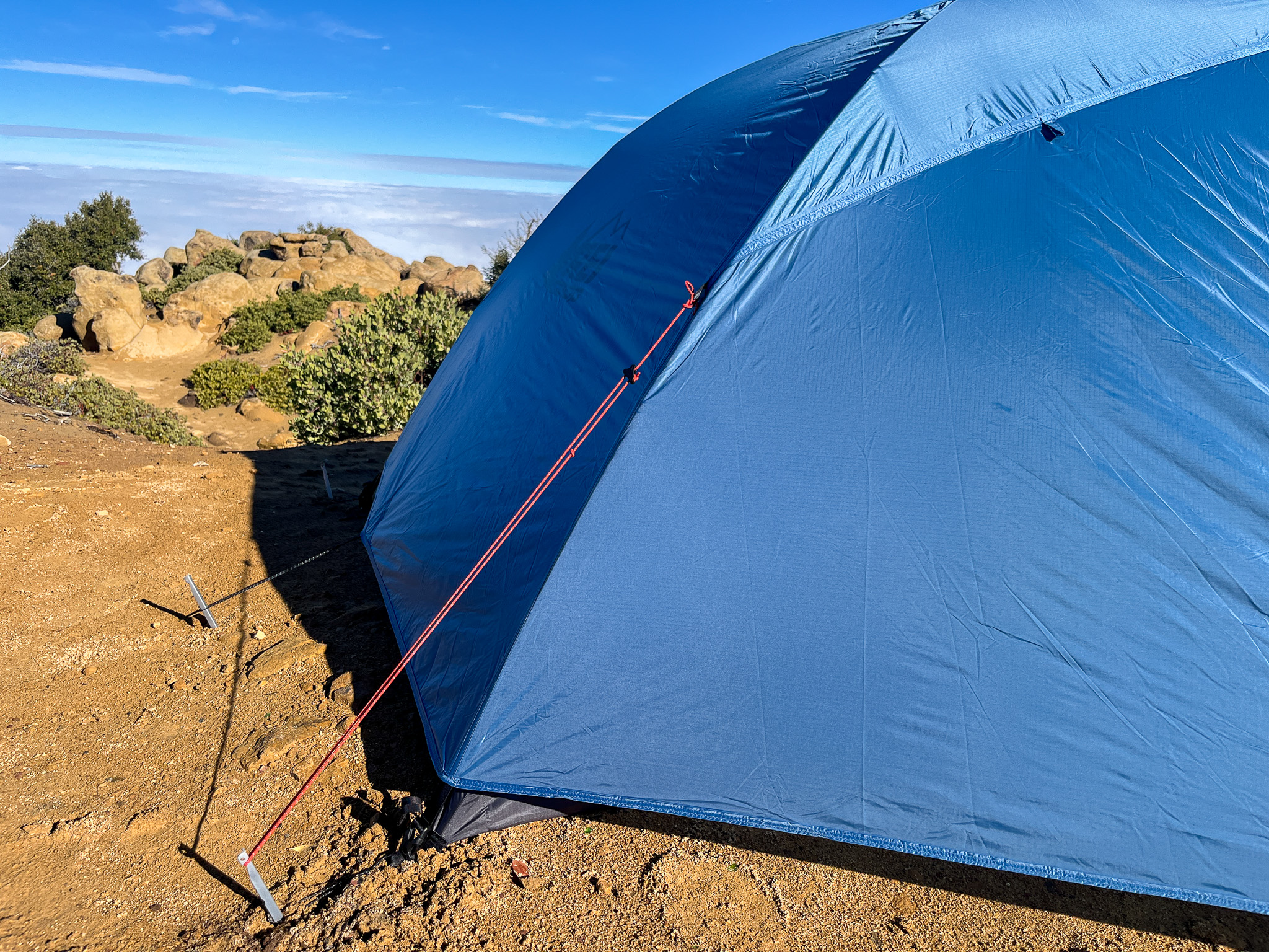 Closeup view of the rainfly fabric and two of the guy out points used for added stability. A pile of rocks and a cloud layer in the background.