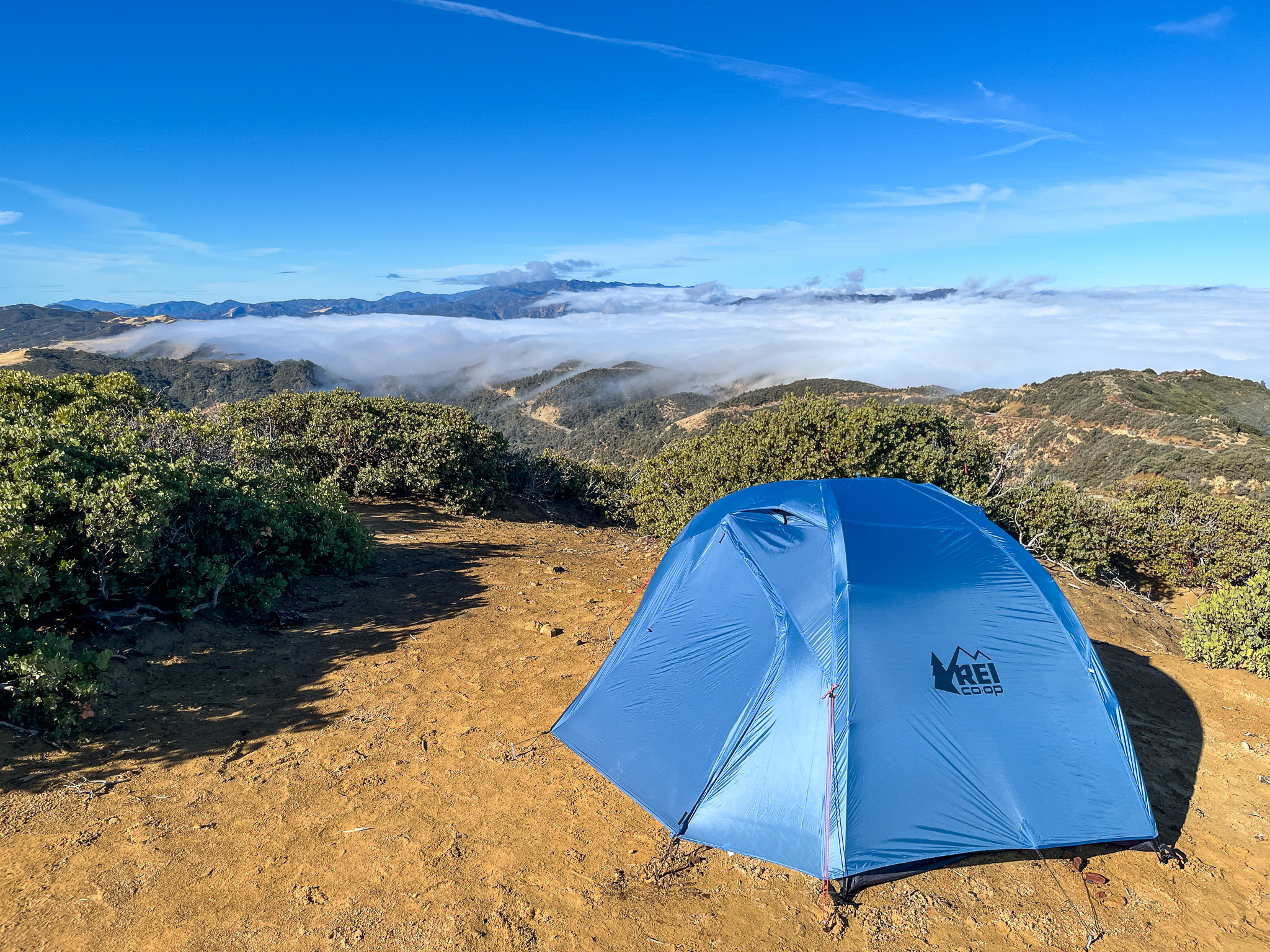 View overlooking blue sky and the mountains with a cloud layer moving across. The REI Half Dome SL2+ pitched in the foreground with rainfly fully zipped up.