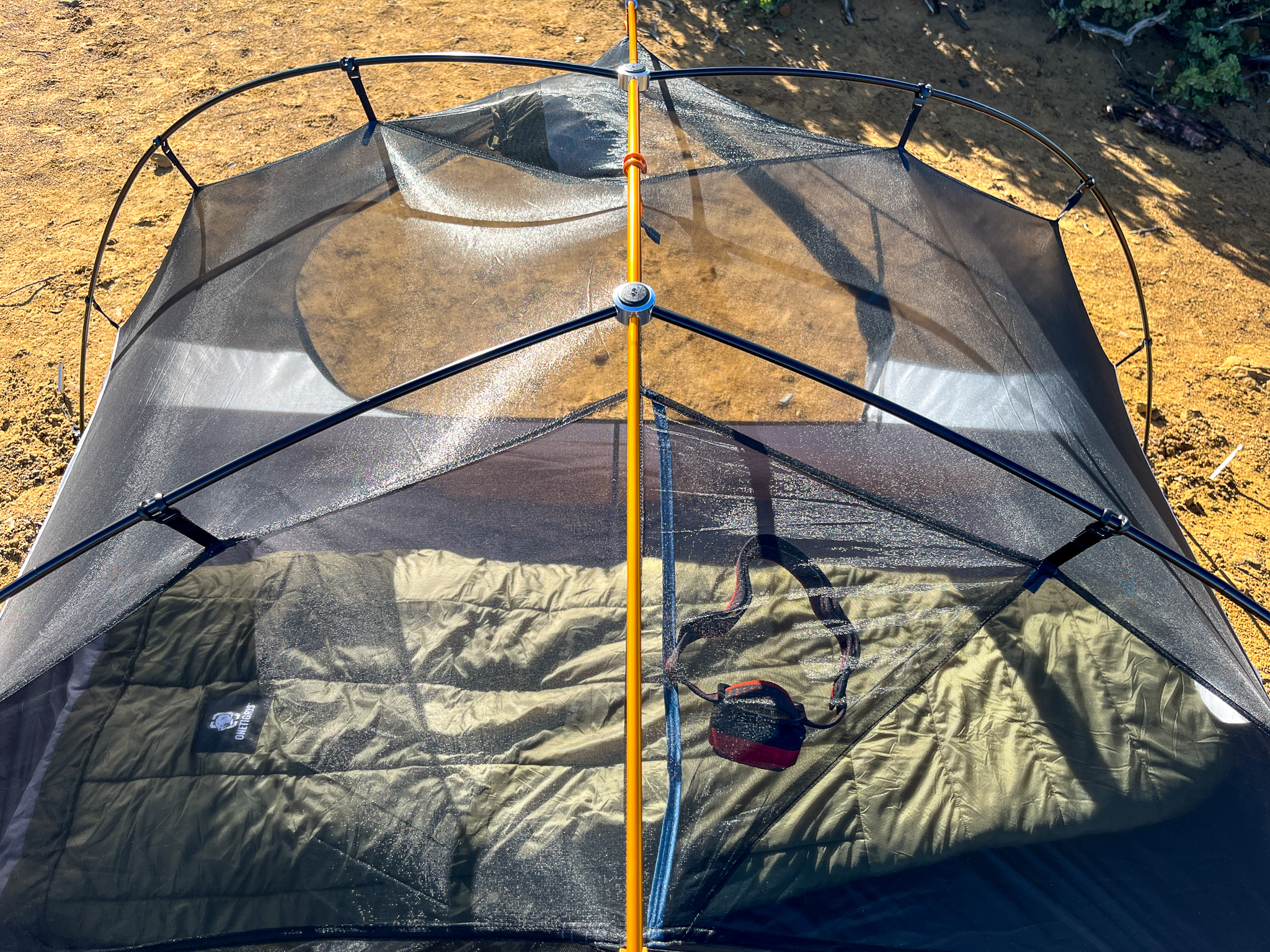 Top view of the REI Half Dome SL2+ showing the pole hub structure. Through the mesh a headlamp is visible in the ceiling pocket, and sleeping bag.