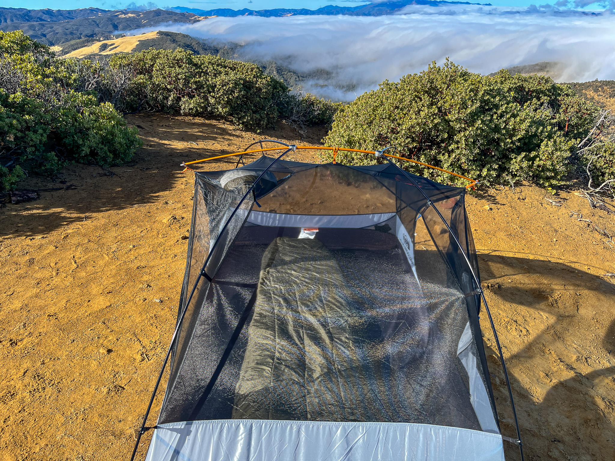 Top view of the REI Half Dome SL2+ showing the pole hub system and integrated ridge bar. Bushes are behind the tent, and mountains with a cloud layer in the background