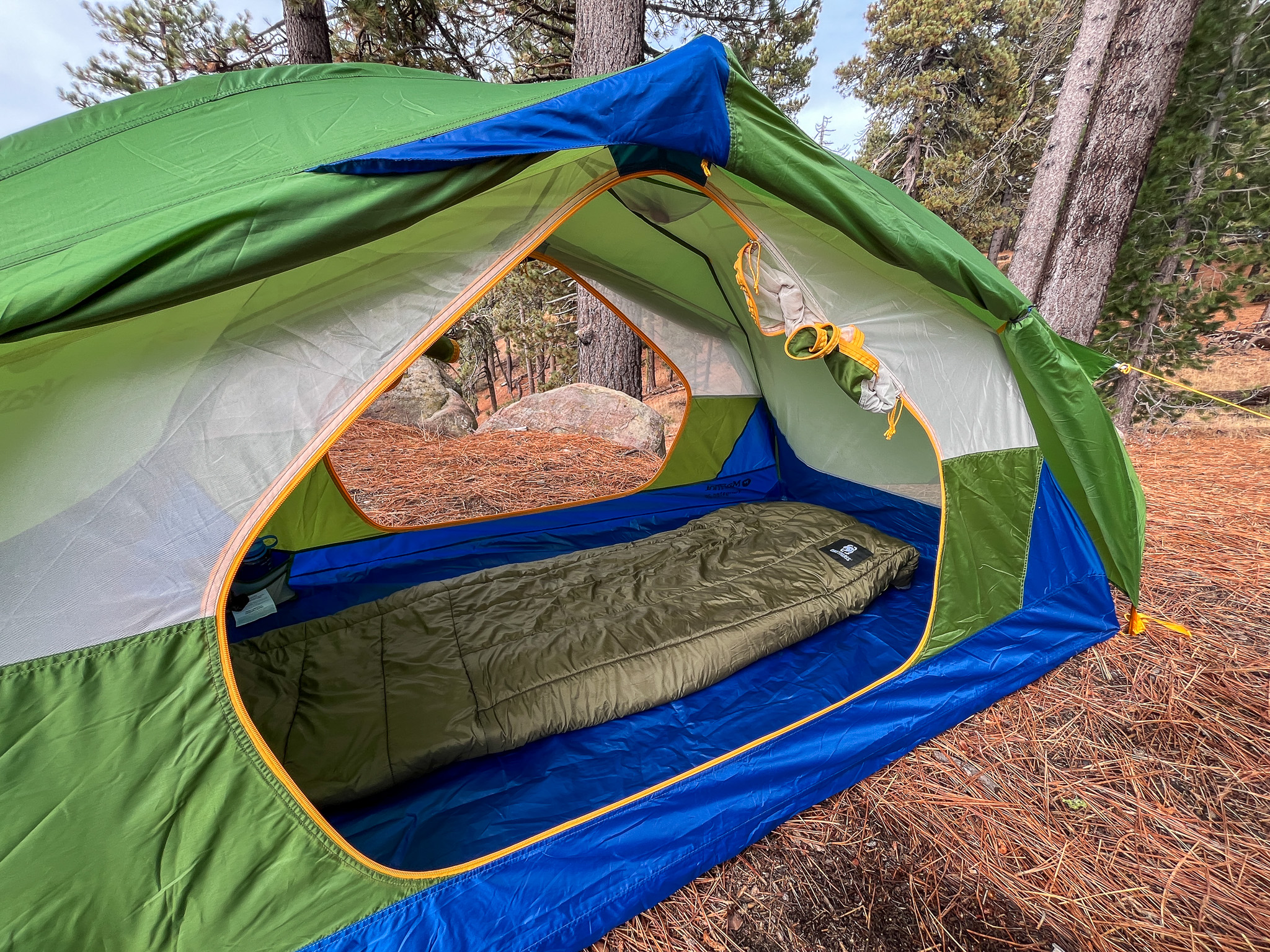 View of the open doors, vestibules, and interior of the Marmot Tungsten 2. Shows a sleeping bag on the inside and surrounding pine forest.