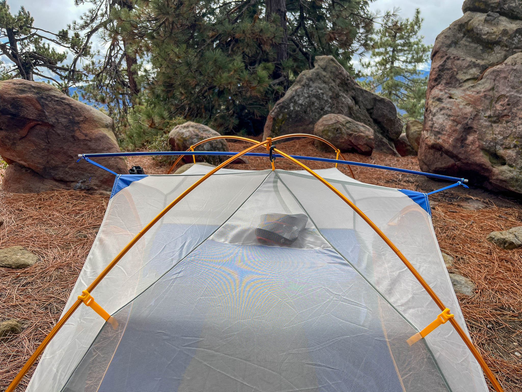 View of the top of the Marmot Tungsten 2's pole configuration. Set up in a forest with large boulders and pine trees.