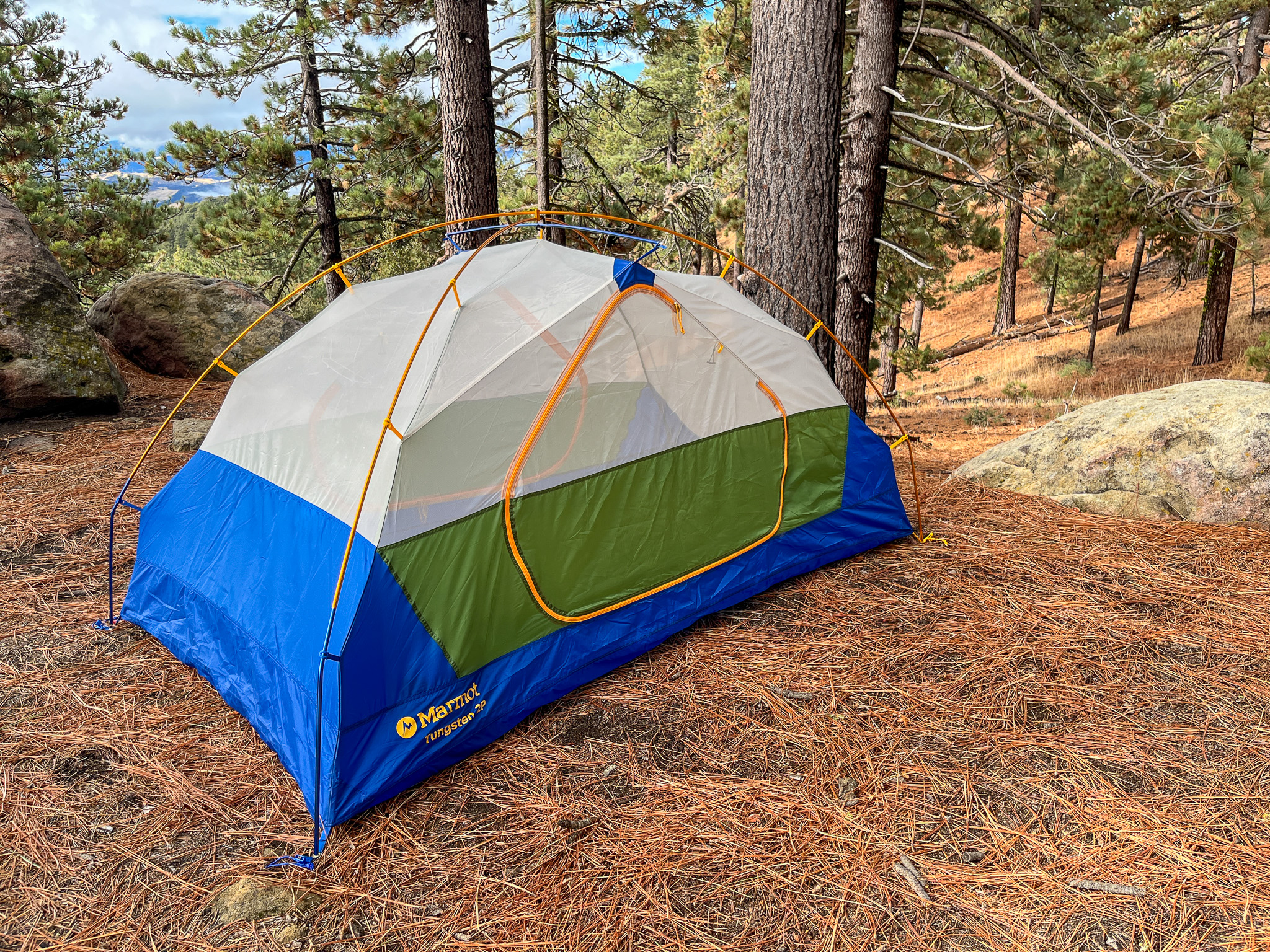 The Marmot Tungsten 2 pitched in on dried pine needles. Tall trees and a distant view of rolling hills visible in the background.