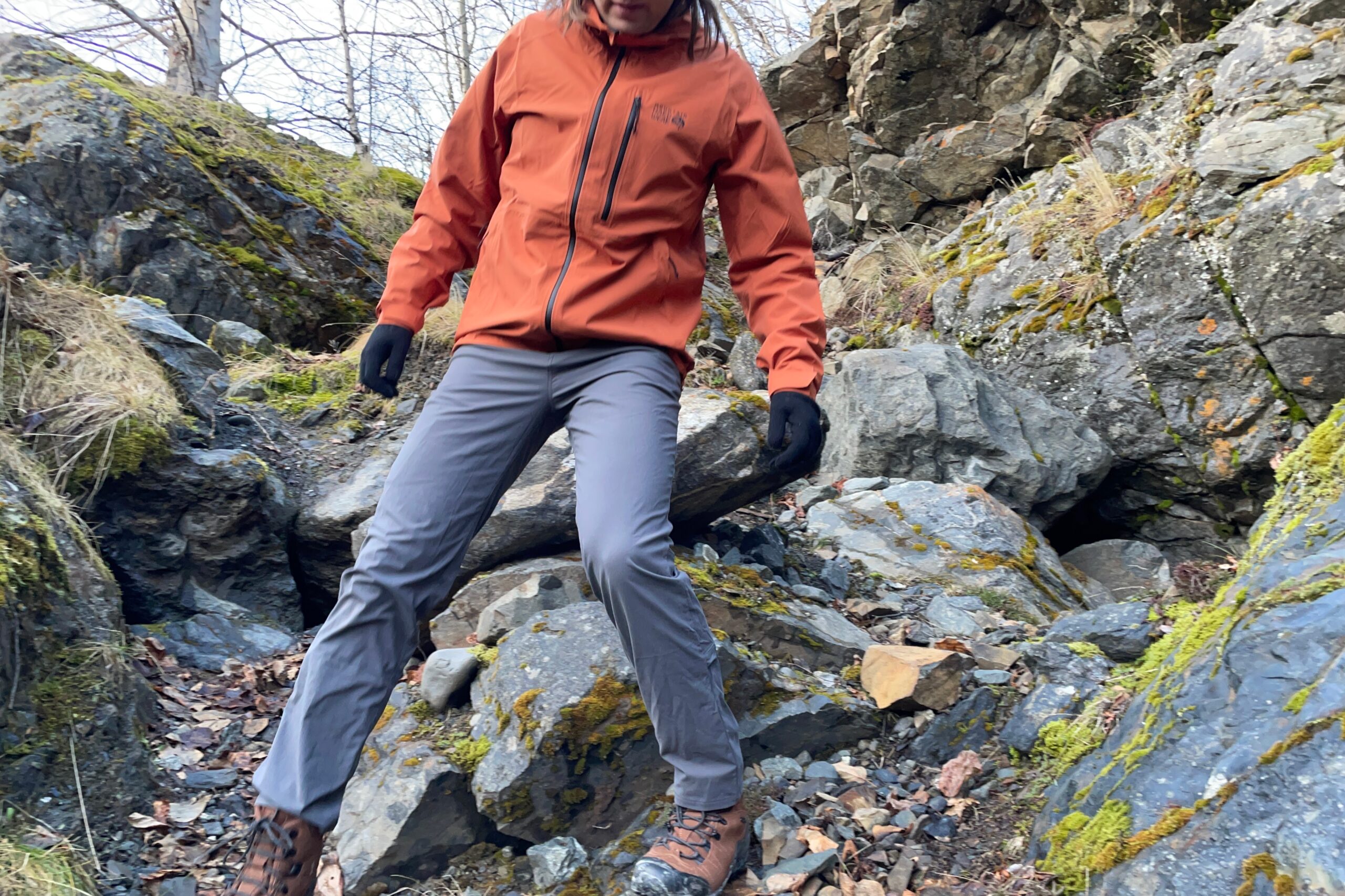 A man walks down boulders on a mossy trail.