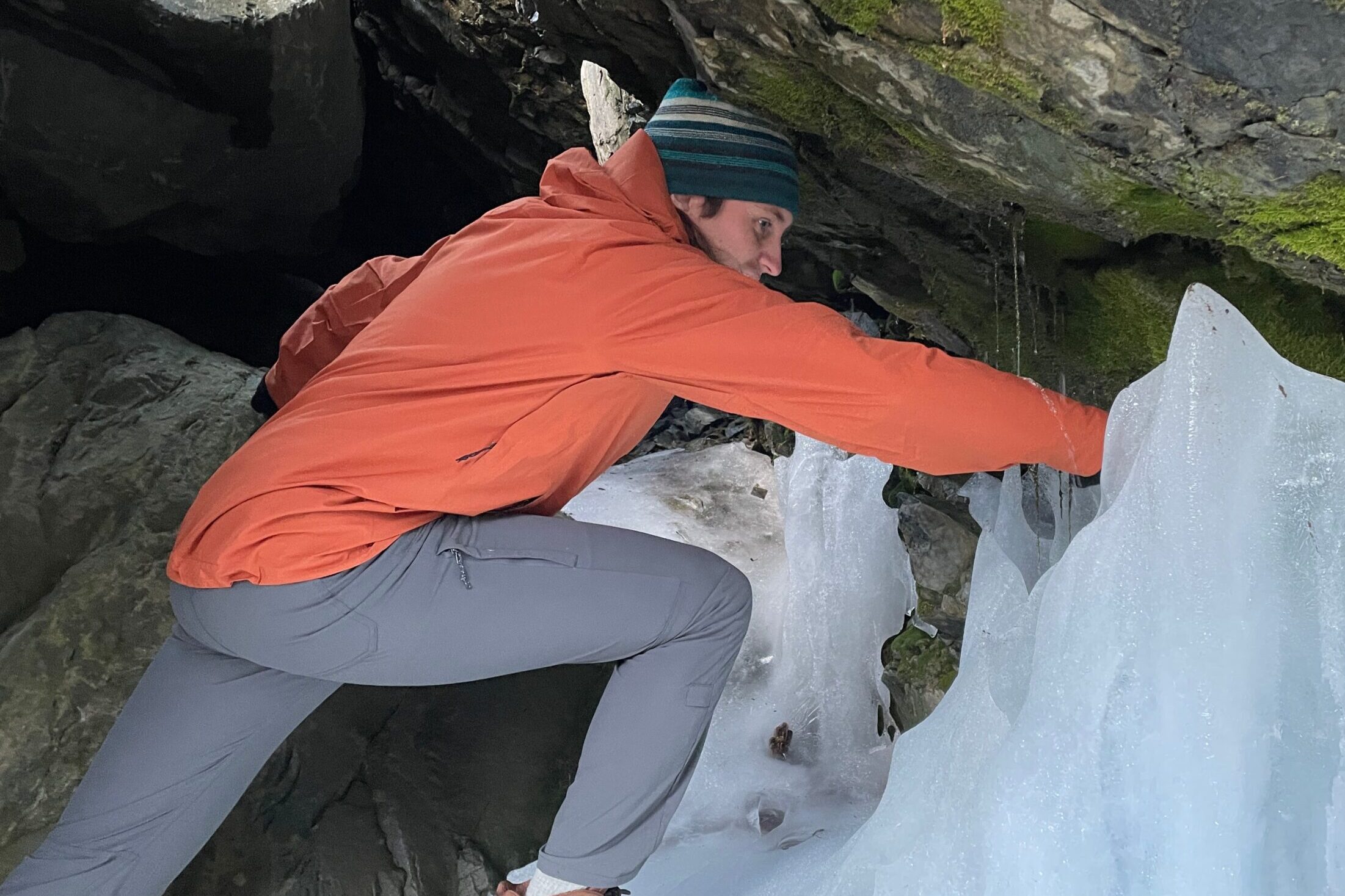 A man reaches in a wet and icy cave.