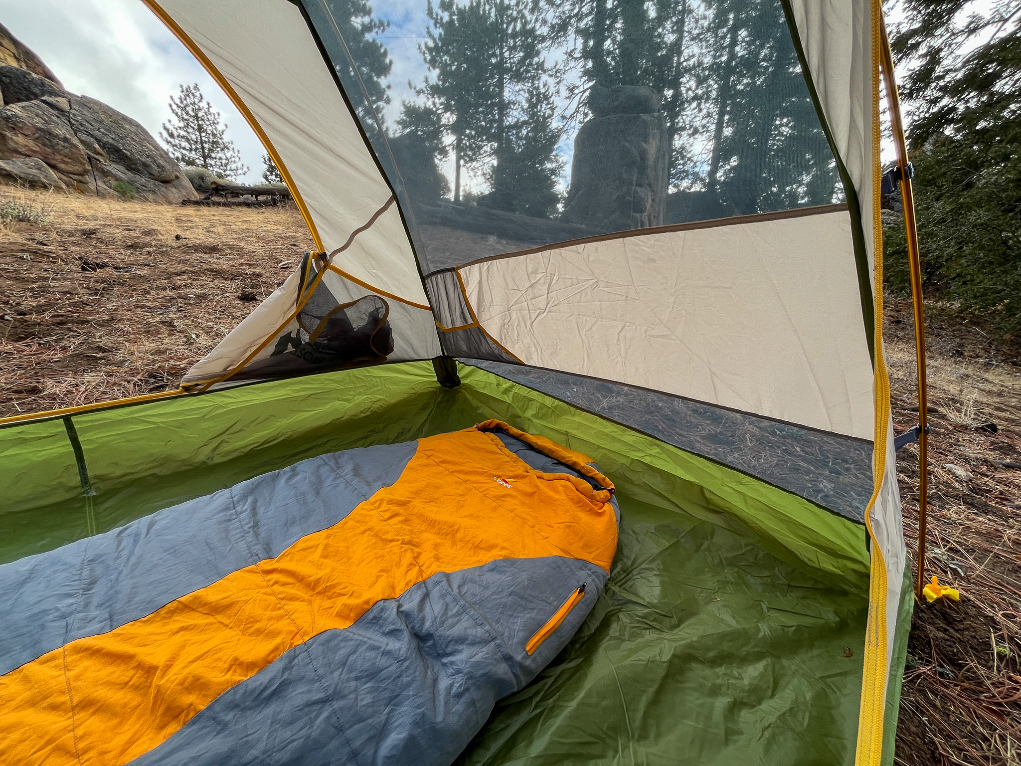 A sleeping bag rests on the floor of the Mountainsmith Morrison EVO 2 tent, with a view of trees and rocks through the mesh wall.