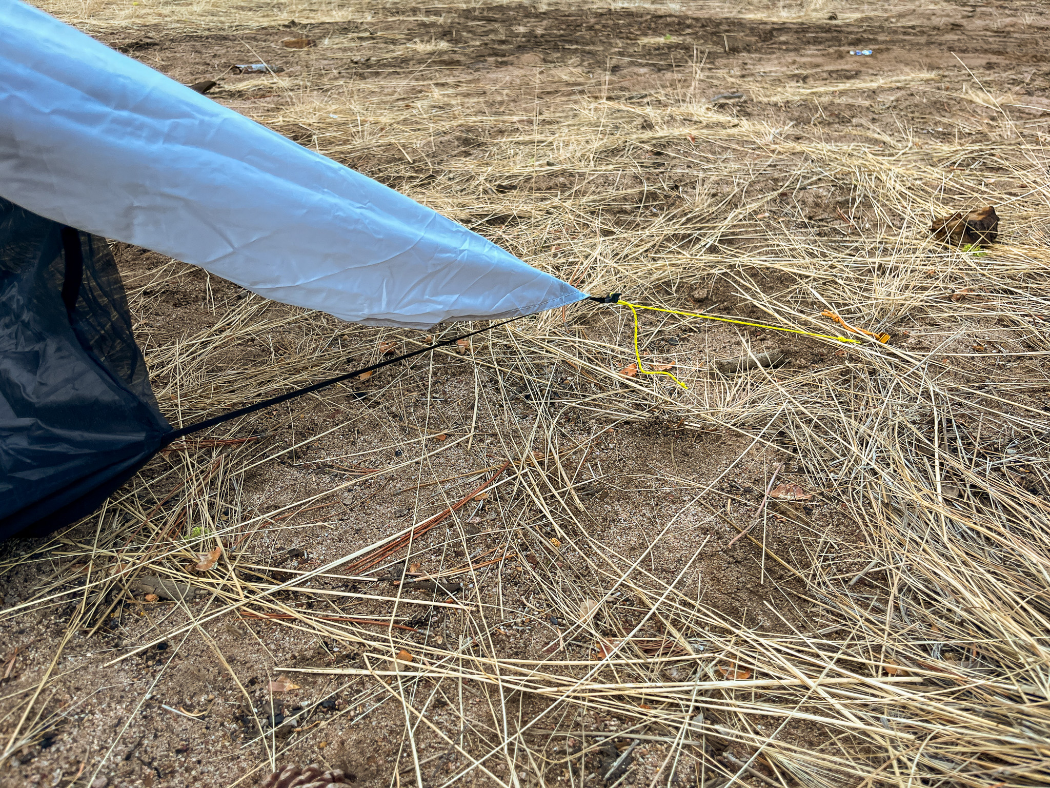 Closeup view of the corner pullout section of the canopy. It's staked out and taut, showing the tension adjuster and shock cord connecting to the inner tent,