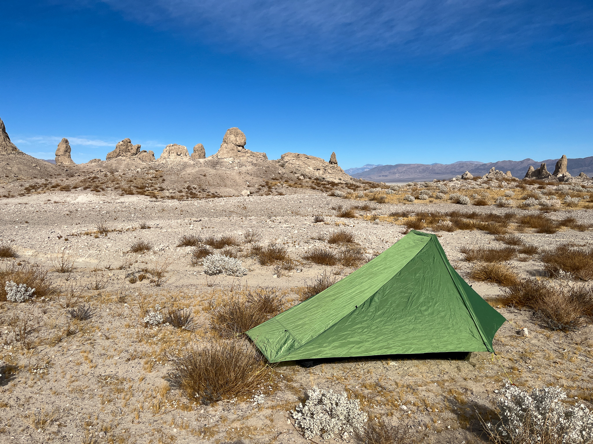 Three-quarter view of the Six Moon Designs Skyscape Scout. It's fully enclosed in the canopy and all guy lines deployed. There's a desert landscape in the background showing a blue sky, big rock pinnacles, dry patches of grass, shrubs, and mountains in the distance.