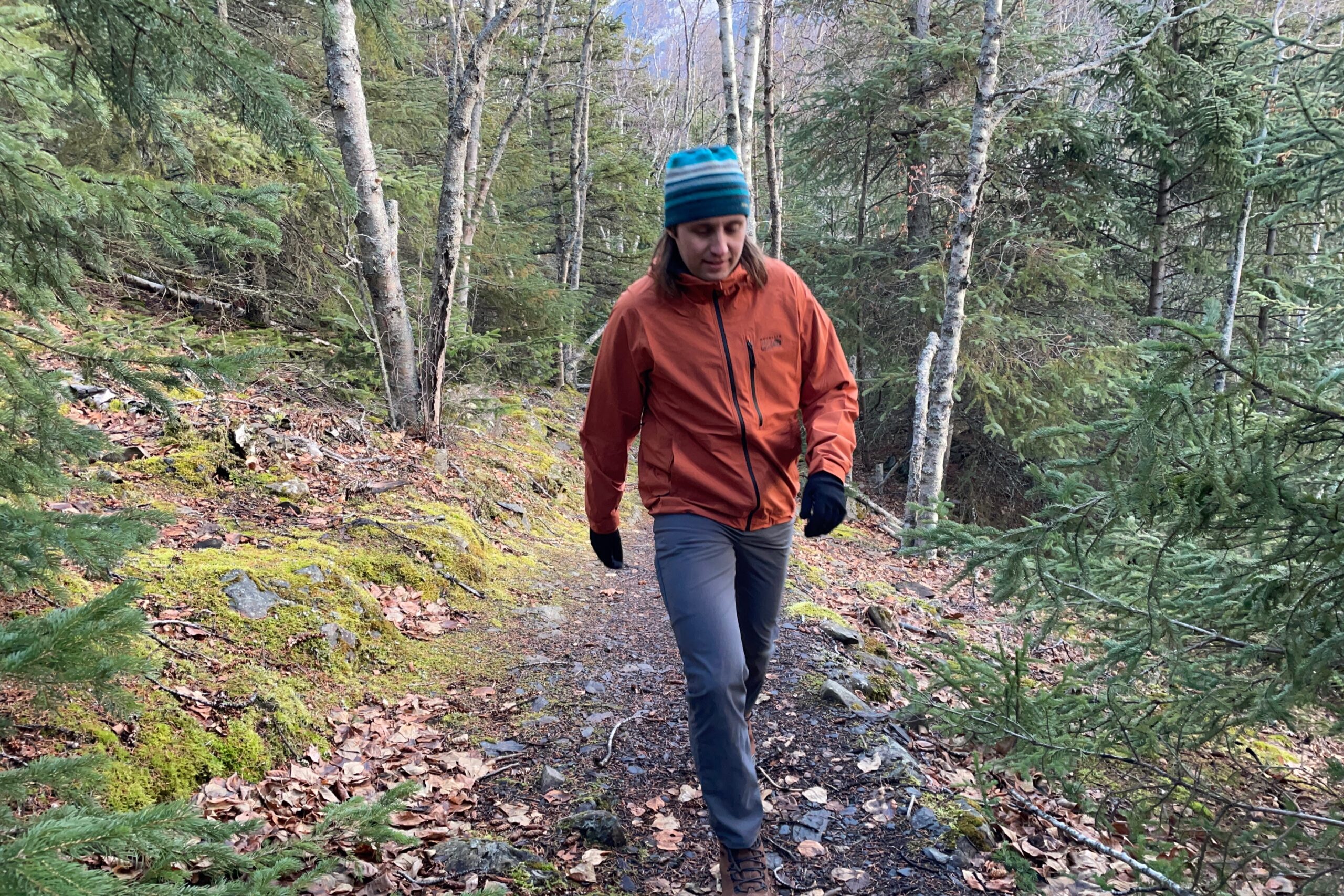 A man walks down a trail wearing an orange rain jacket.