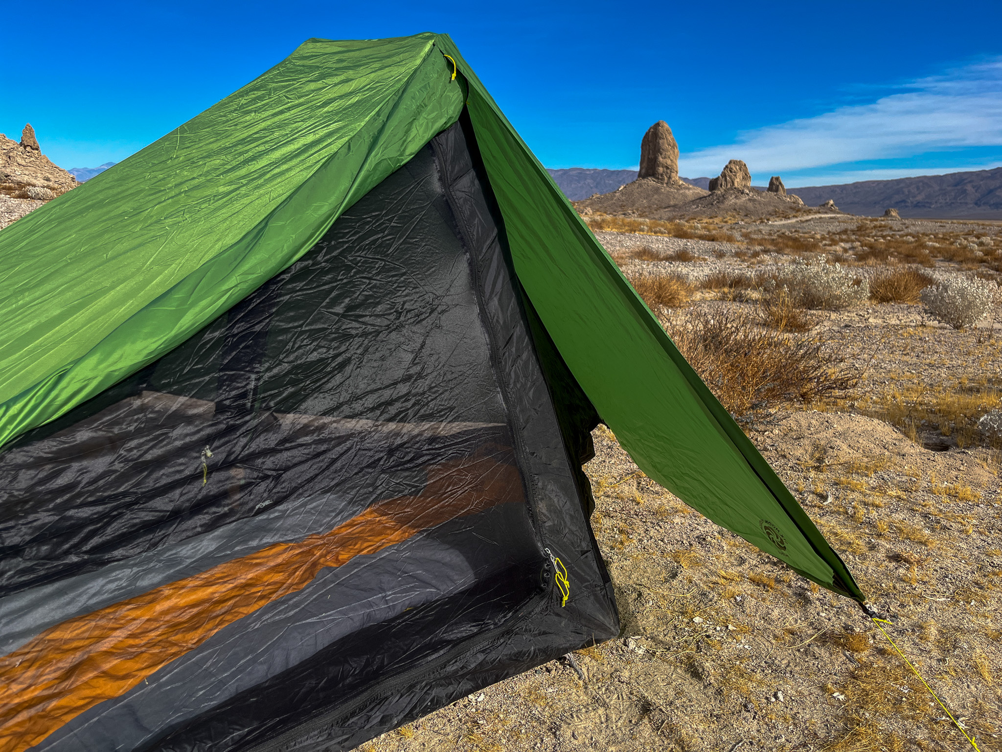 A view of an open vestibule with the other portion tied back, and sleeping bag visible through the inner mesh. Desert landscape and distant mountains in the background.