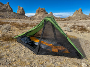 View of the Six Moon Designs Skyscape Scout with the vestibules and inner door rolled back showing a backpack and sleeping bag inside. Large rock pinnacles and desert landscape in the background.