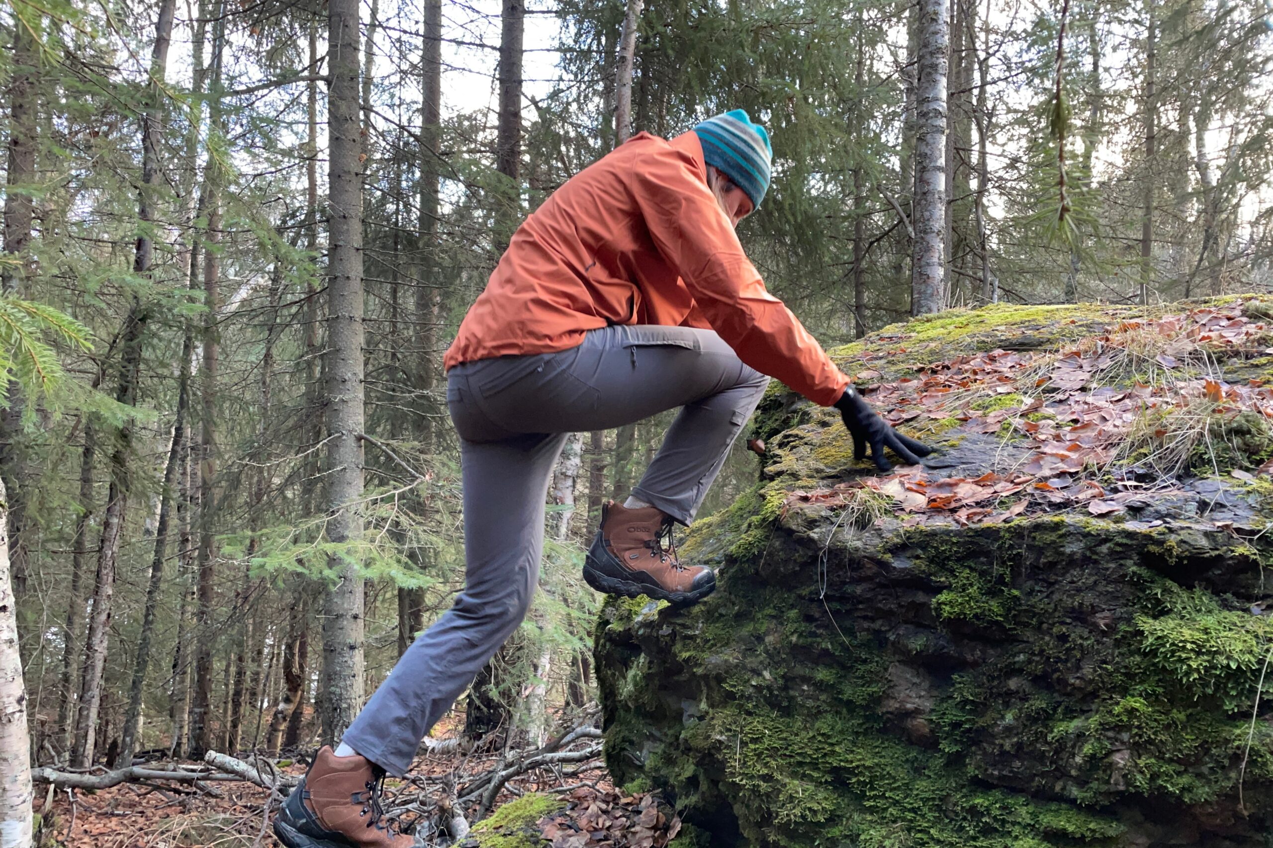 A man scrambles up a mossy boulder.