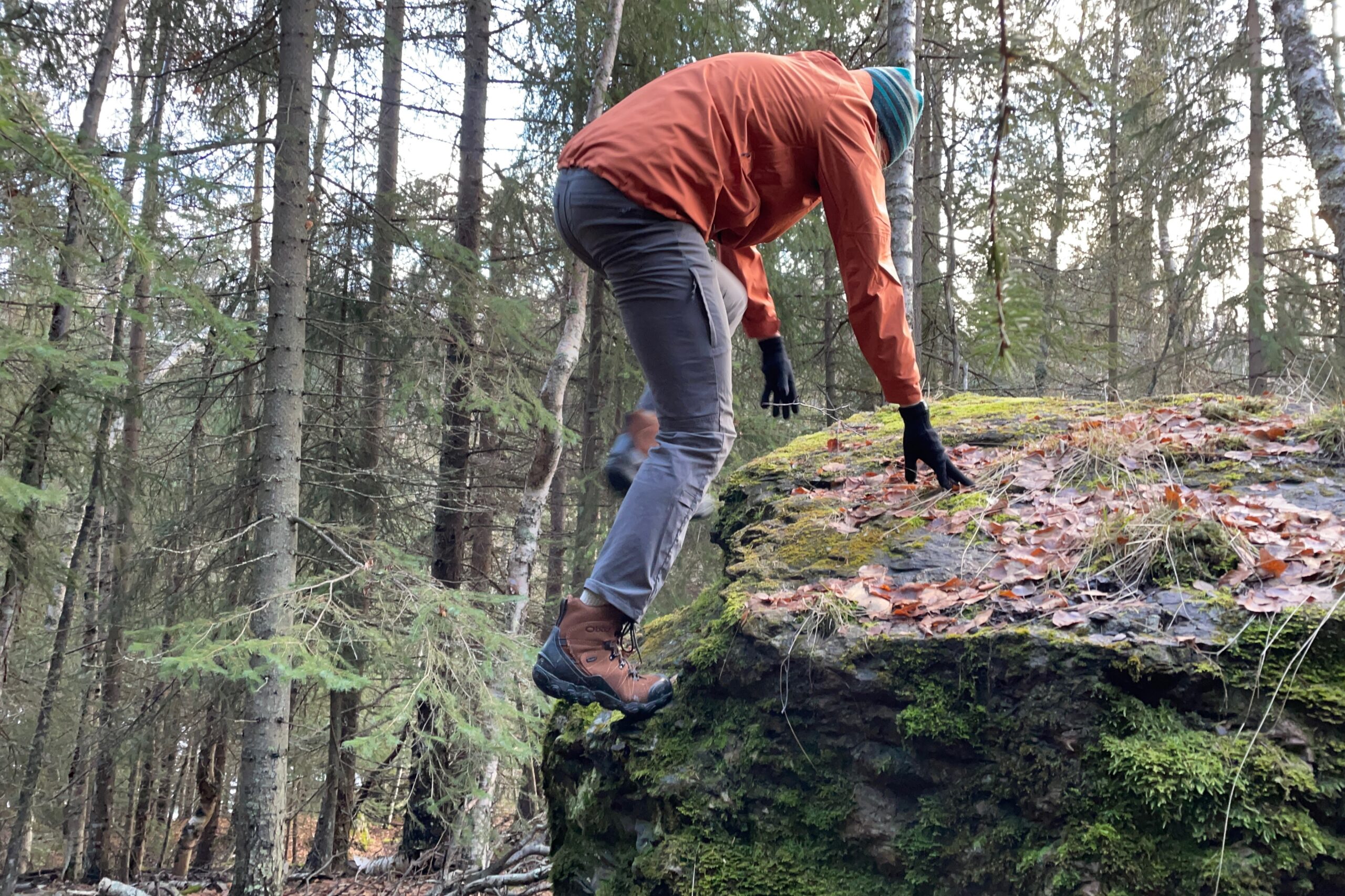 A man clambers up a mossy boulder.