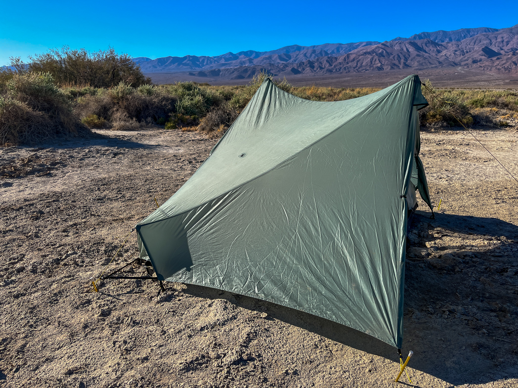 Side view of the Tarptent Stratospire 2 showing the sloping panels of the rainfly. Desert bushes, blue sky, and distant mountains in the background