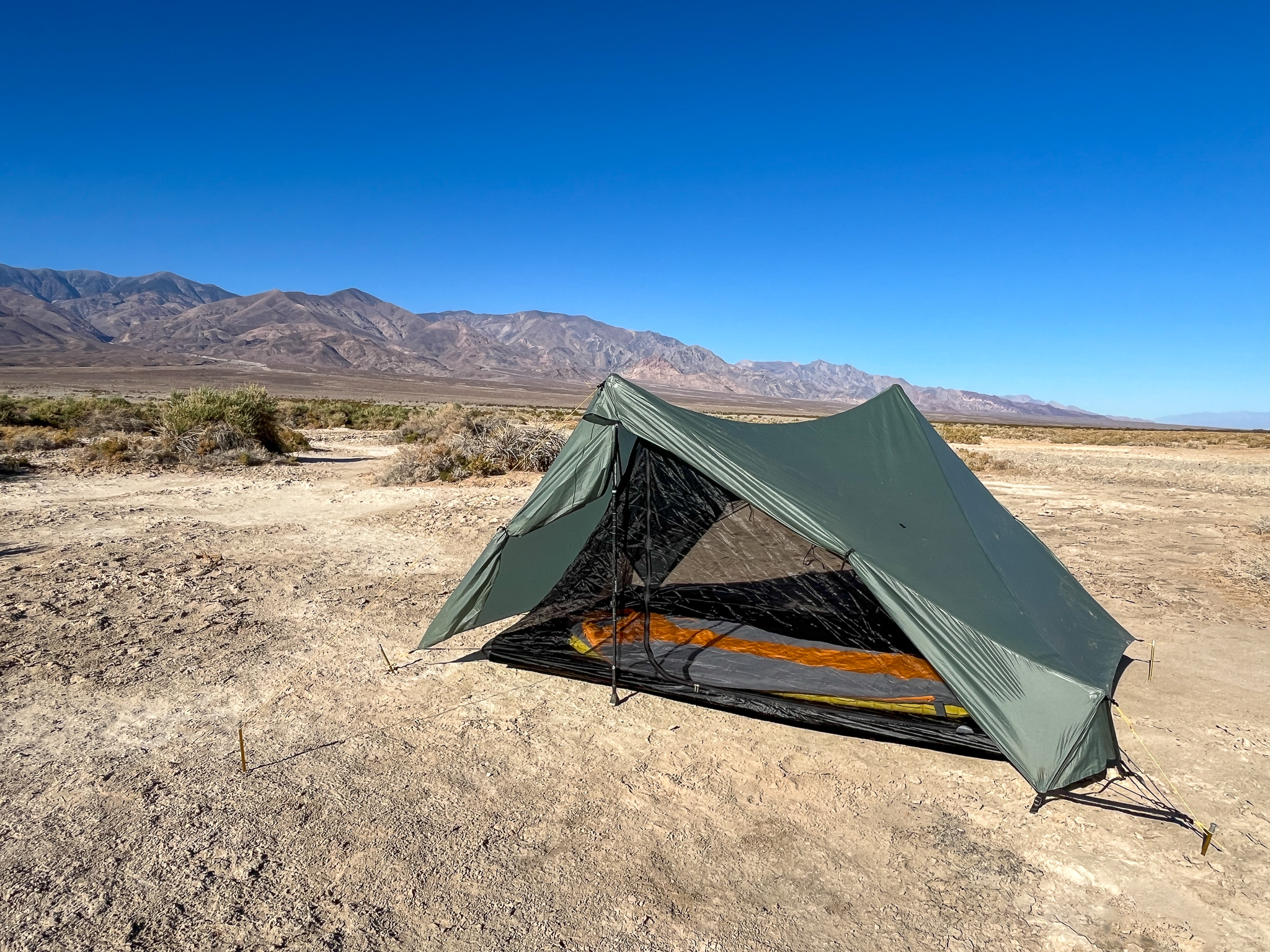 The Tarptent Stratospire 2 pitched with vestibule doors rolled up and sleeping bag visible through the inner mesh. Desert landscape with blue sky and mountains in the distance