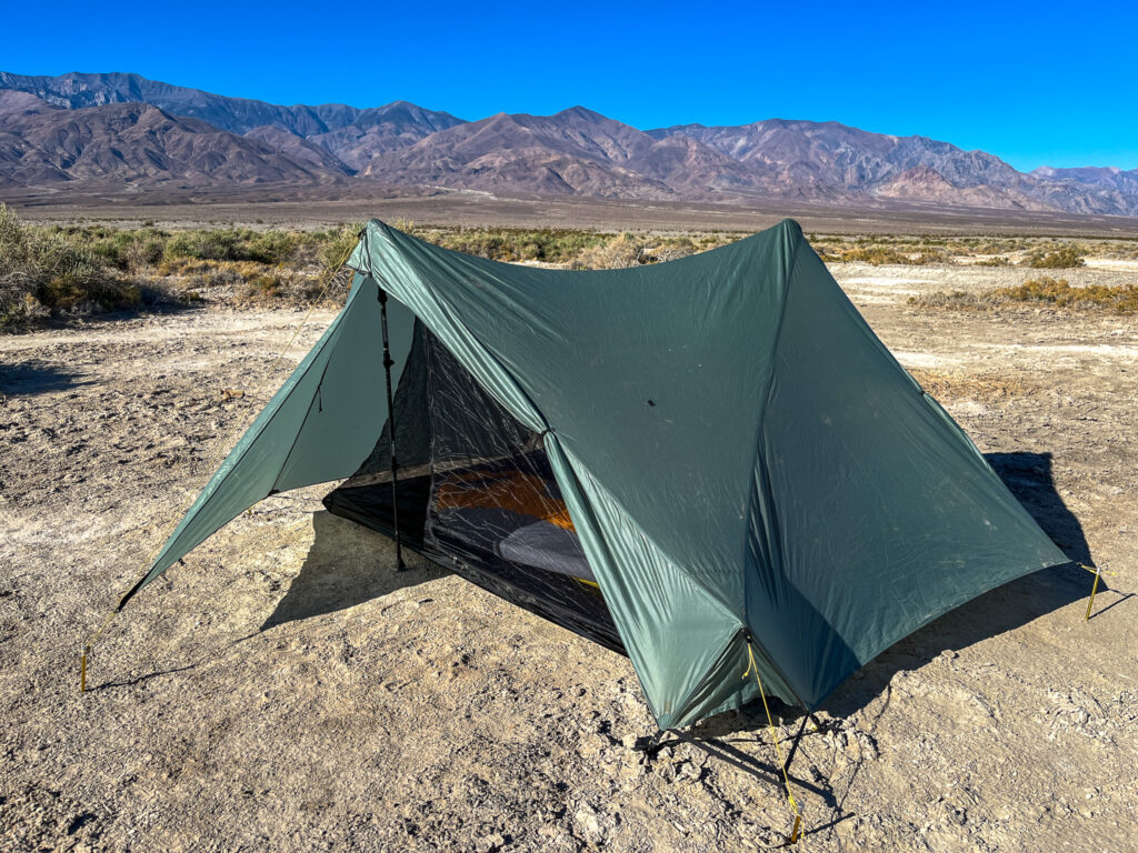 The Tarptent Stratospire 2 pitched with the rainfly and one vestibule door open, revealing the inner mesh and sleeping bag inside. Desert landscape with distant mountains in the background.