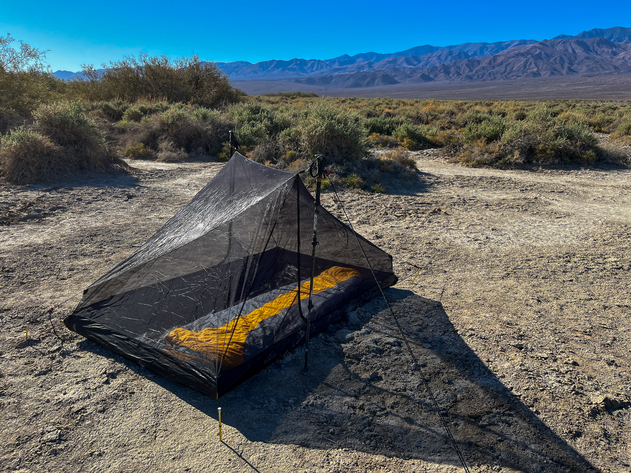 View of the Tarptent Stratospire 2's inner mesh portion pitched with two trekking poles and thick guy line. High desert and mountains in the background.