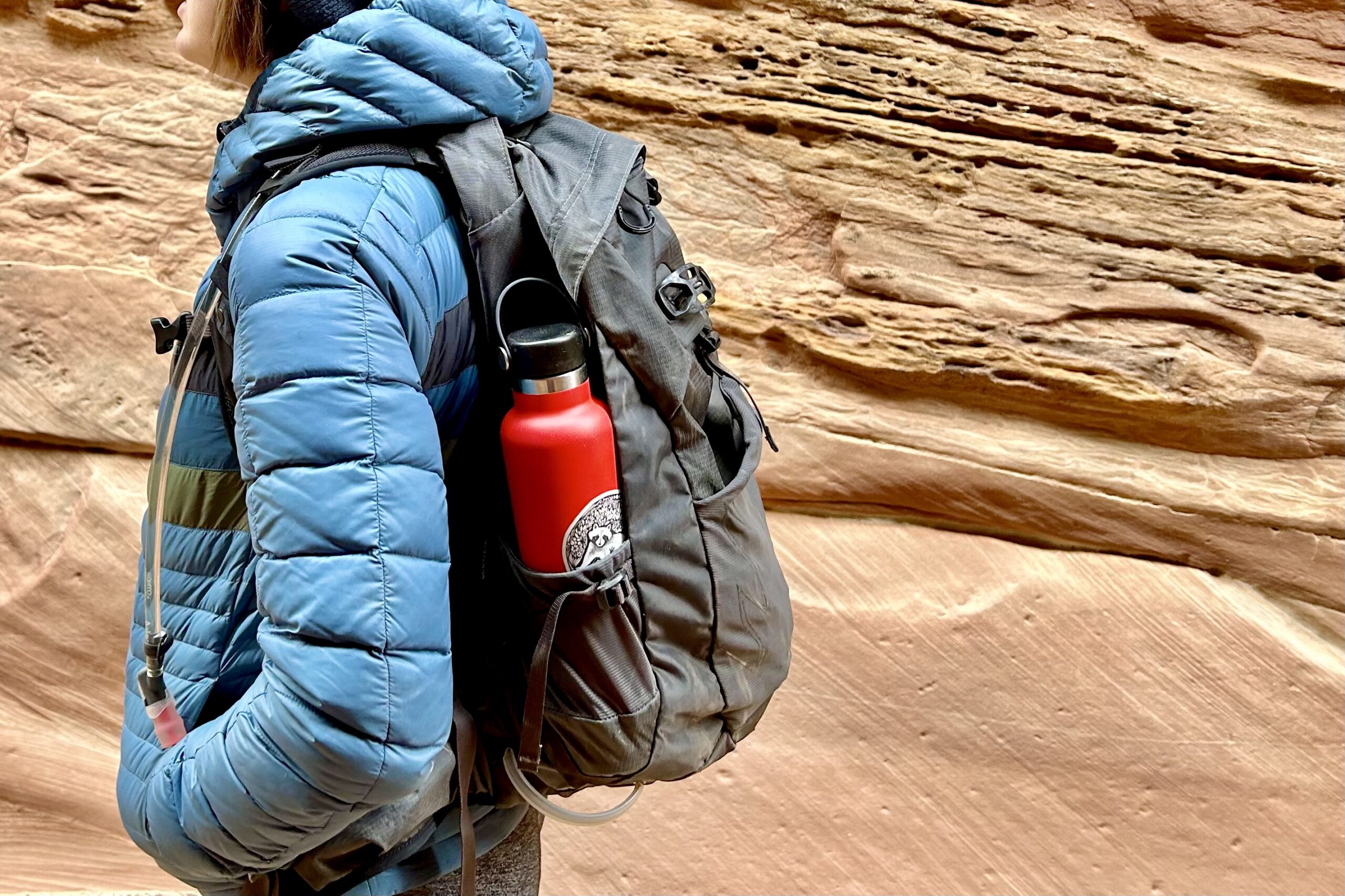 Close up image of a person hiking through a canyon wearing a daypack smeared with mud.