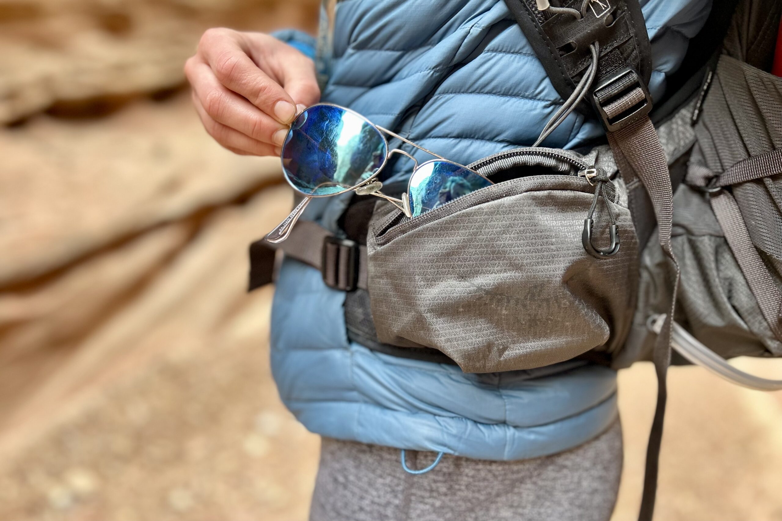 Close up image of a person pulling sunglasses out of a waist strap pocket.