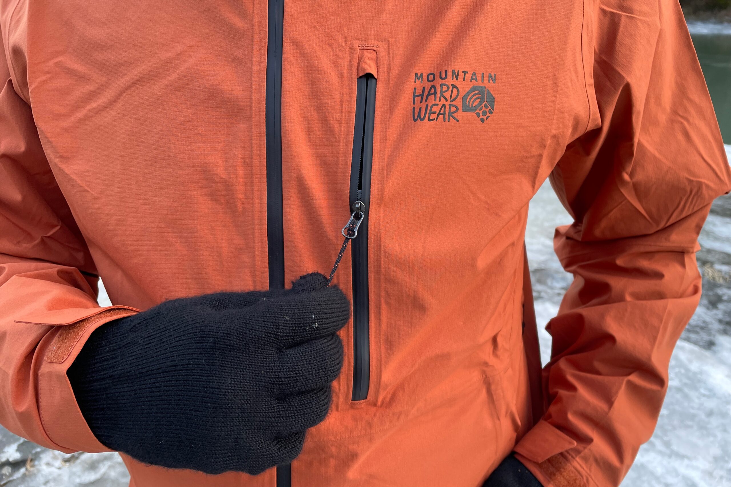 A man unzips the chest pocket of his rain jacket.