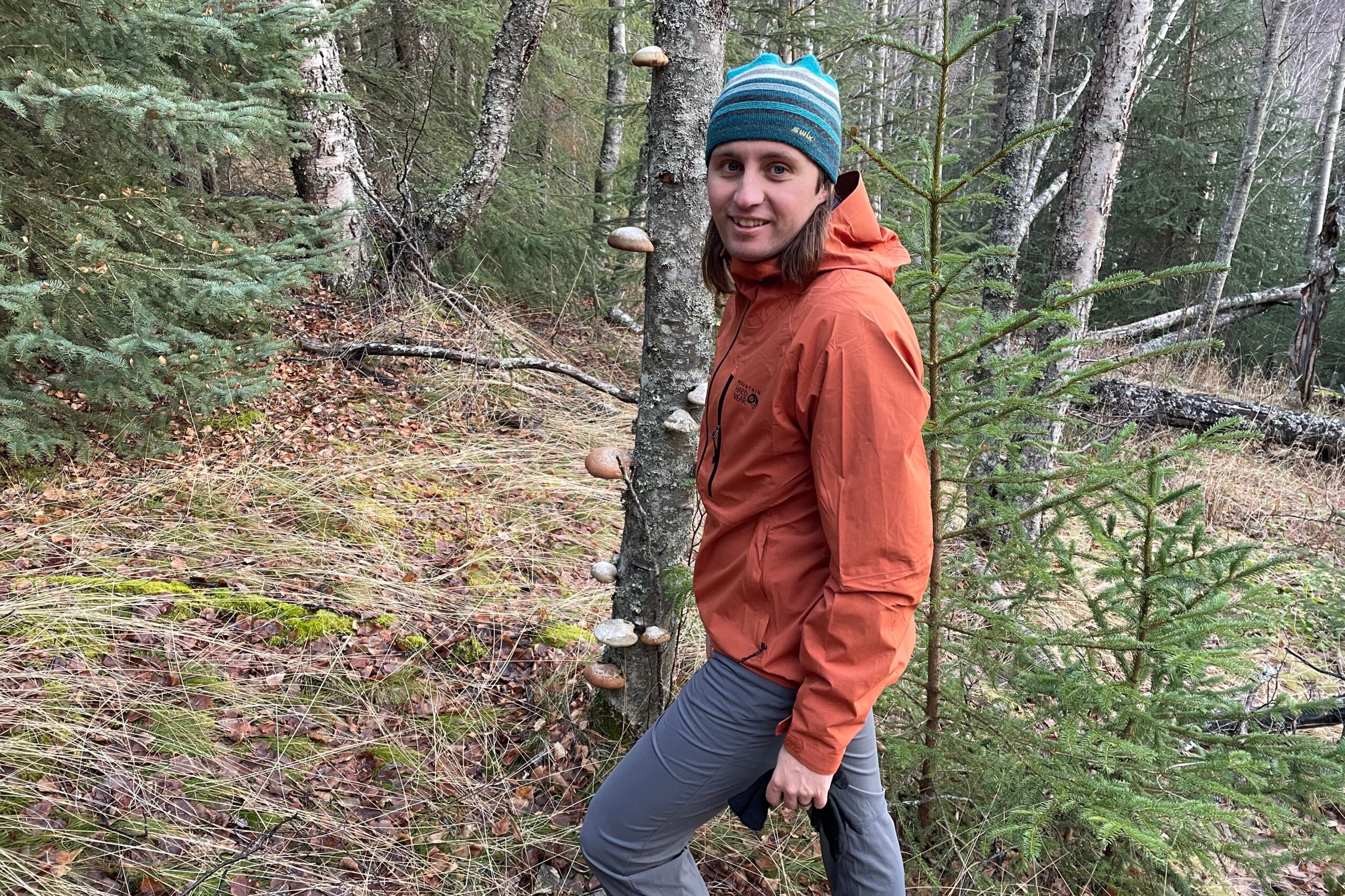 A man stands in the forest wearing an orange rain jacket.