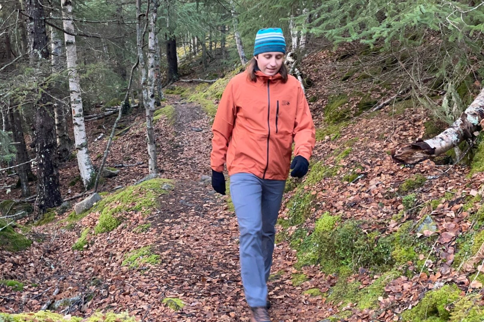 A man walks through a forest trail wearing an orange rain jacket.