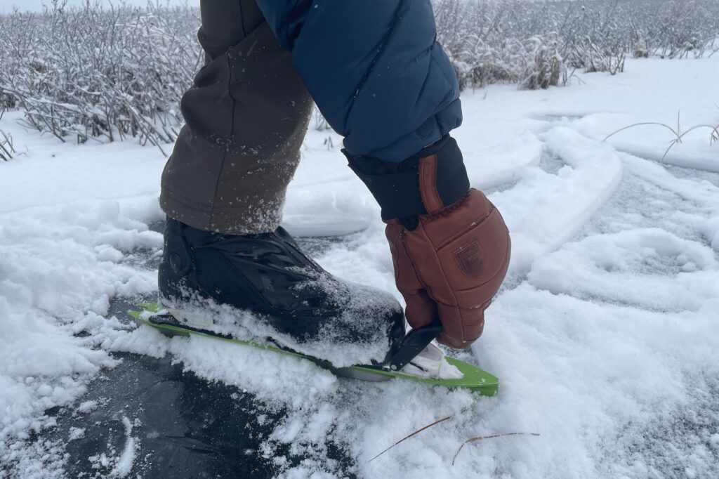 A man puts on ice skates while wearing gloves.