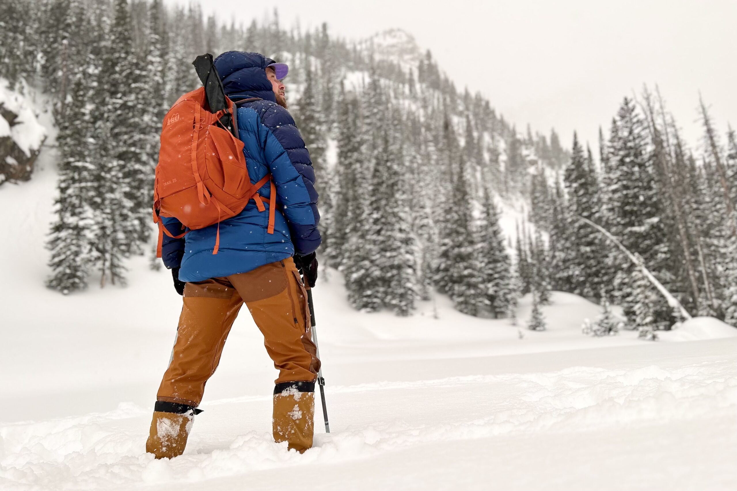 A man in winter gear hikes through deep snow in a field.