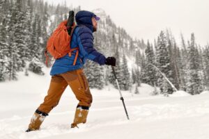 A man in winter gear hikes through deep snow in a field.