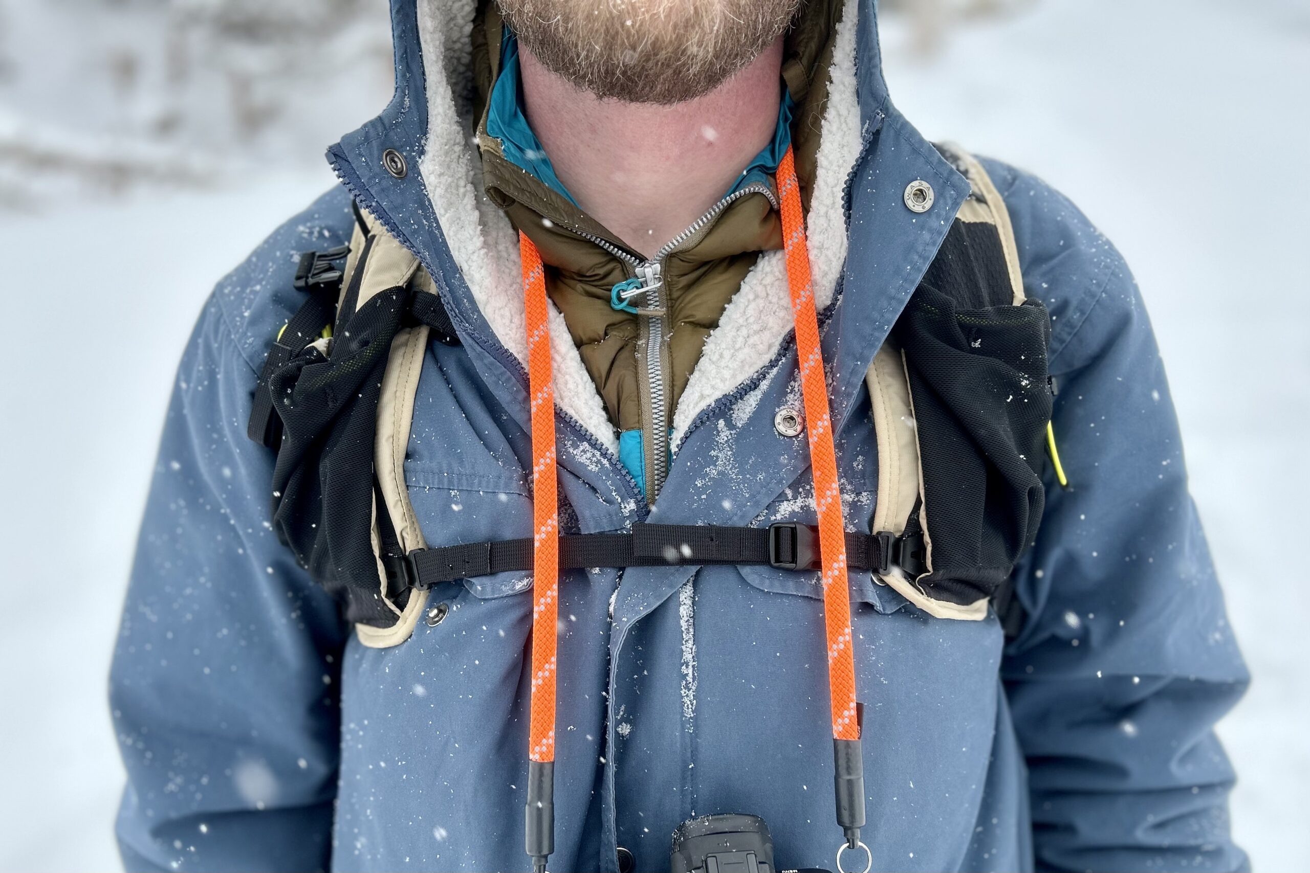 Close up of shoulder straps as a man hikes through a wintry scene.