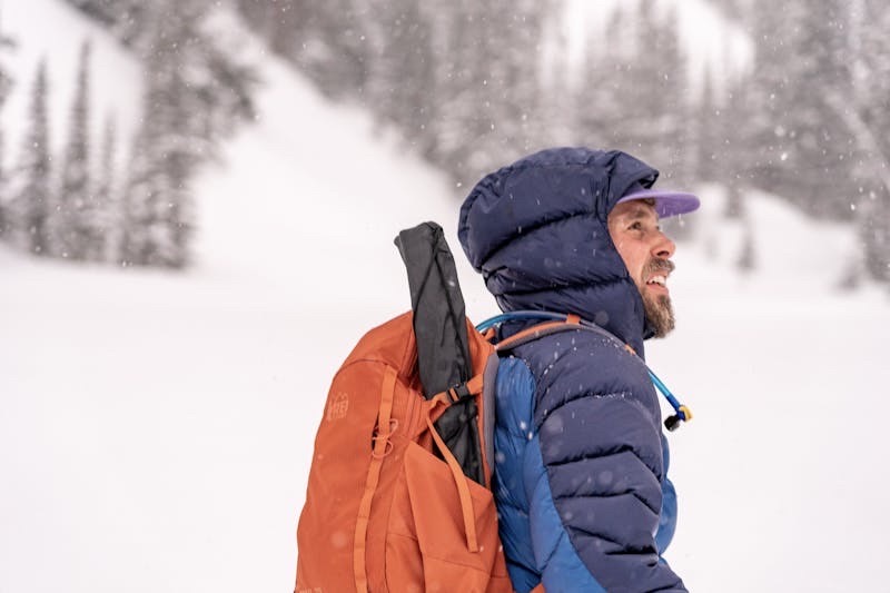 A man with winter gear on looks into the distance in a snowstorm.