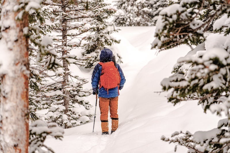 A man in winter gear hikes through deep snow in the mountains.