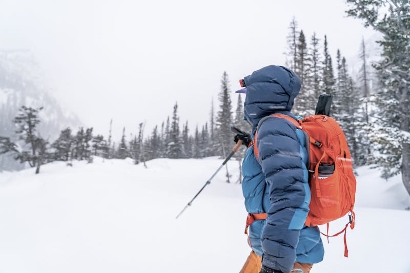 A man in winter gear hikes through deep snow in the mountains.