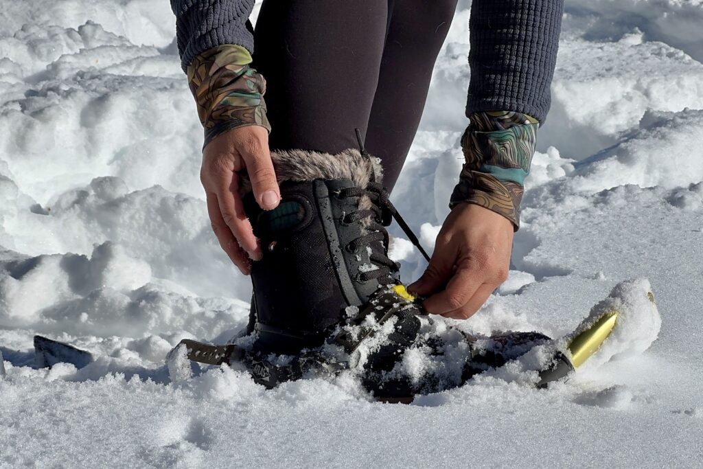 Close up of a person adjusting some straps on a pair of snow shoes while wearing the Bogs Arcata in the snow.