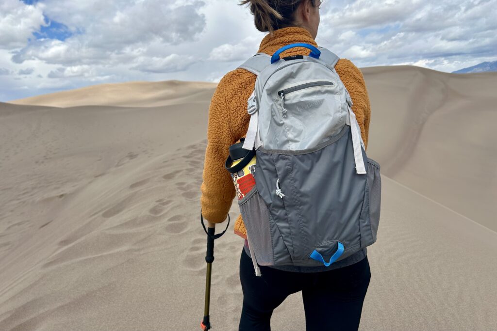 A woman walks through sand dunes on a stormy day with a backpack on.