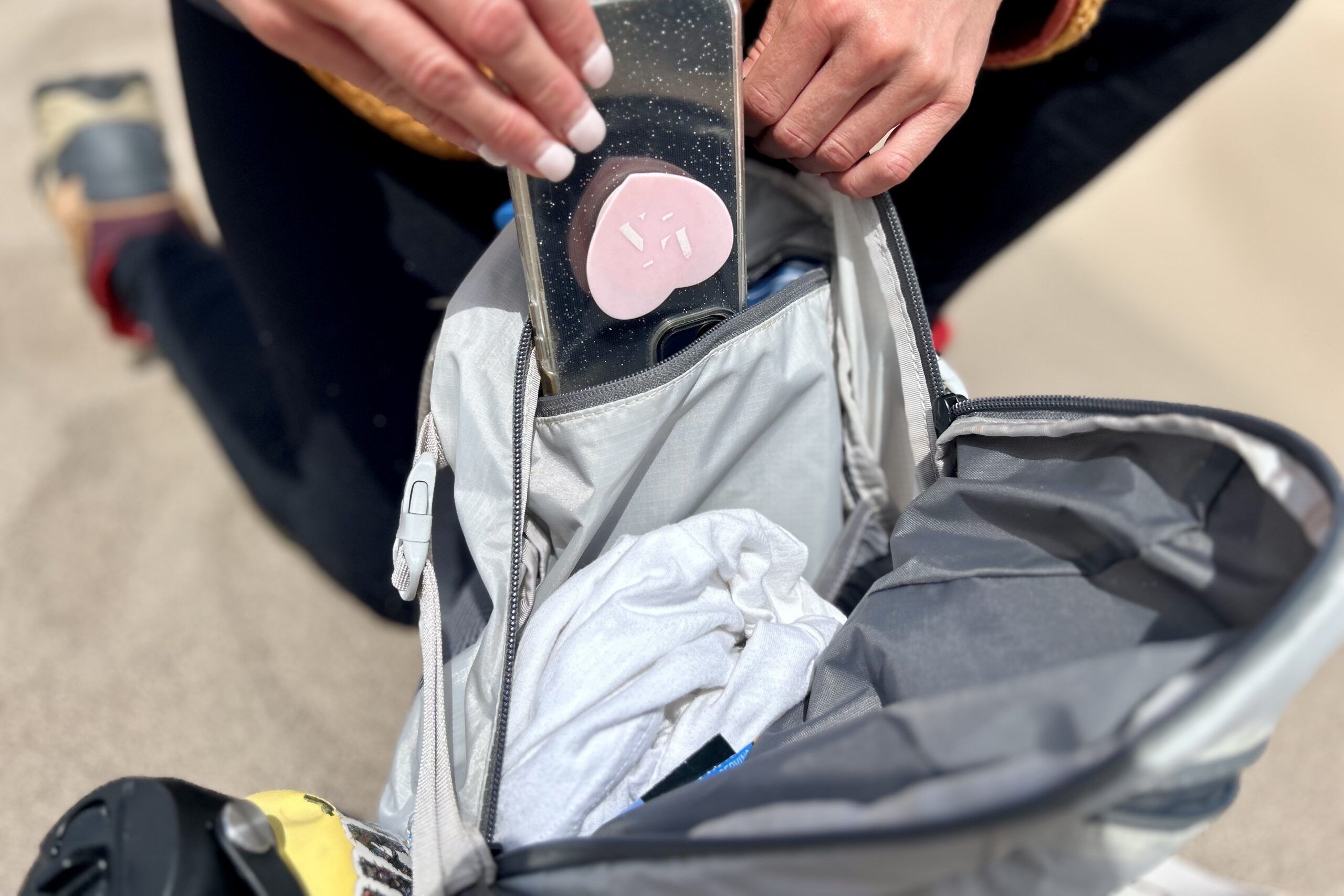 Close up of a person putting a phone into a zippered backpack pocket.