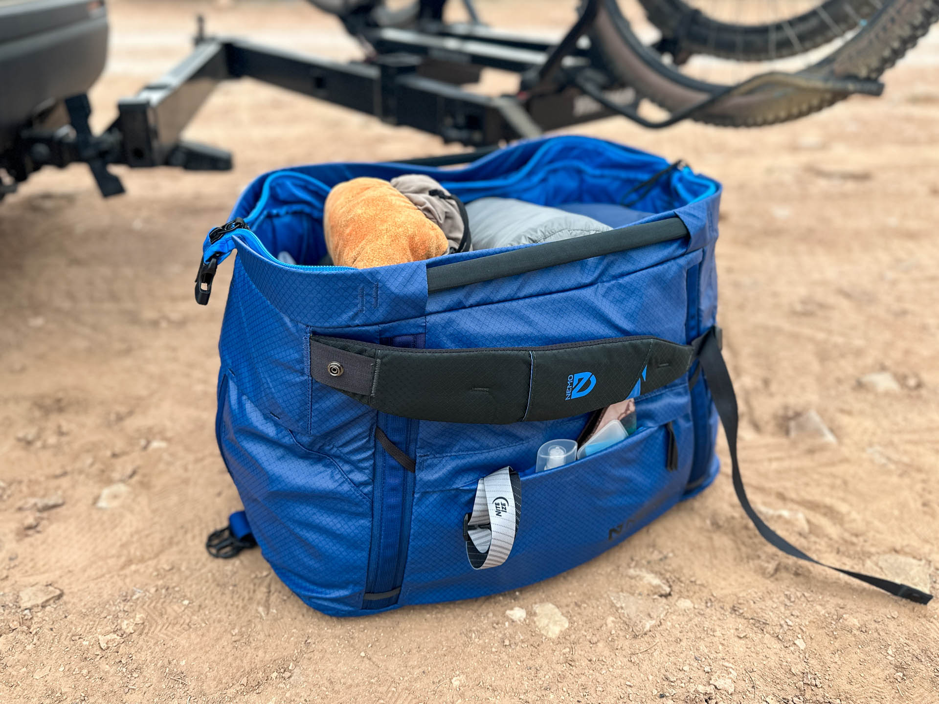 The Nemo Double Haul duffel packed with camping gear in gear hauler mode sitting on the ground in front of a bike rack.