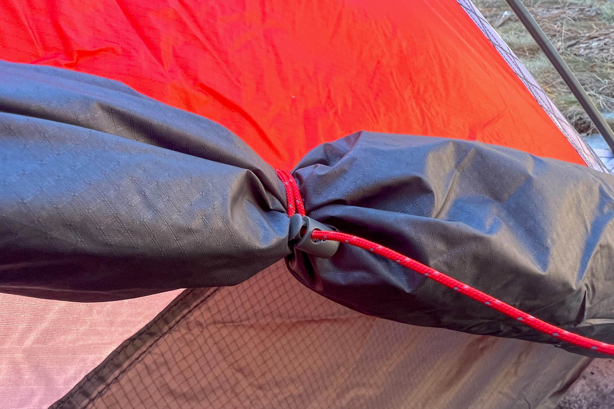 Close-up of a red tent’s rainfly secured with a toggle and red guyline, showing its attachment system.